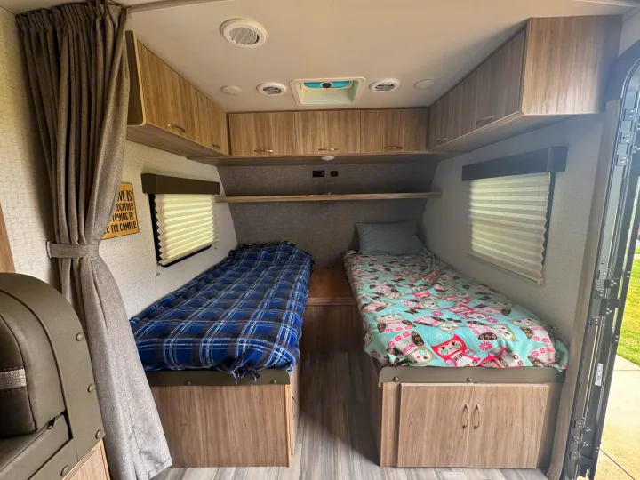Inside a comfortable RV rental: two twin beds with blankets, overhead cabinets, and windows with blinds.. Minnie Micro Minnie 2021