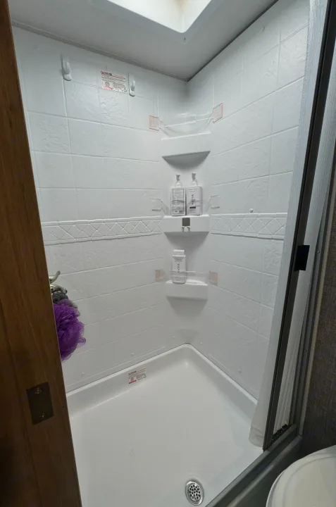 Inside an RV rental shower: white walls, built-in shelves with Native toiletries, and a loofah. Practical and compact.. Minnie Micro Minnie 2021