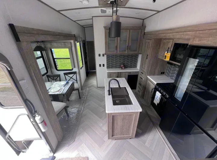 Modern RV rental interior: spacious light wood kitchen with island sink, black appliances, and a dining area.. Forest River Salem Hemisphere 2022