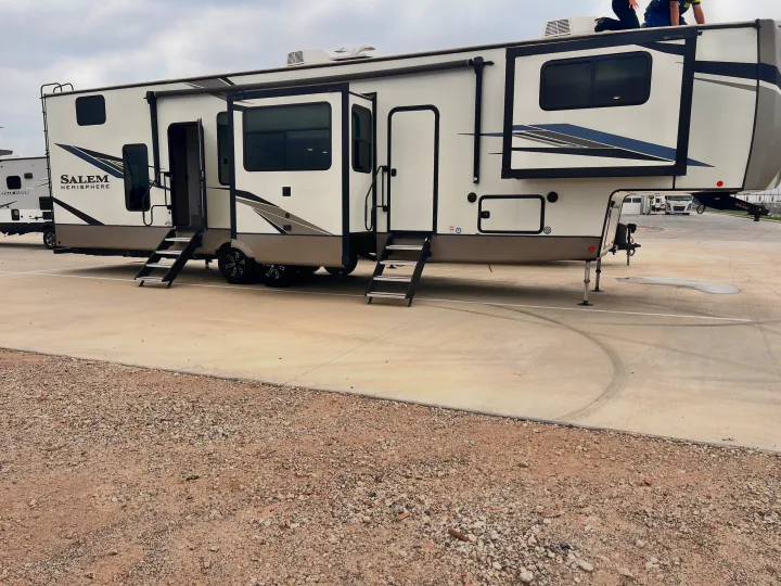 A large white and gray Salem Hemisphere fifth-wheel RV with extended sections and steps, on a lot, ready for rv rental.. Forest River Salem Hemisphere 2022