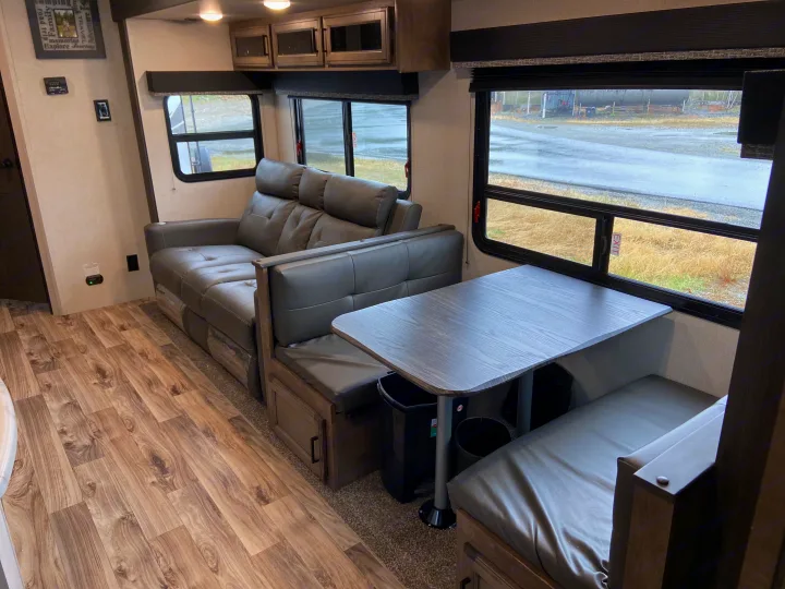 Inside an RV rental: a modern gray sofa, convertible dinette, and wood floors for comfortable travel.. Venture Sport Trek 2021