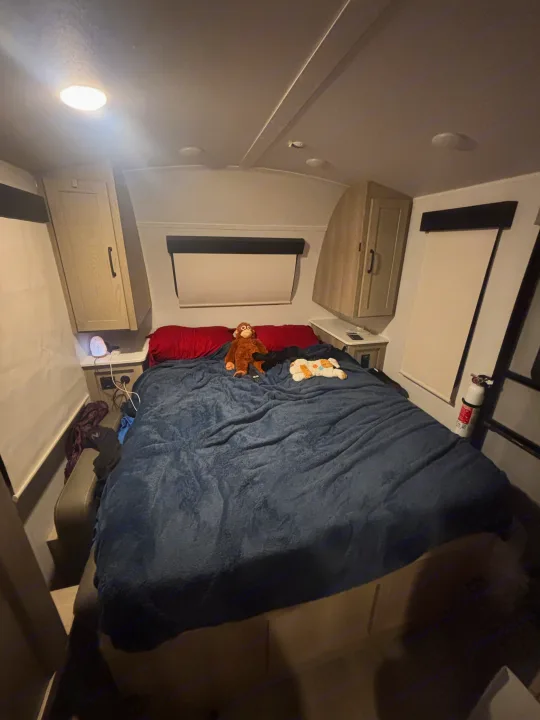 Cozy RV rental bedroom with a large bed, blue blanket, stuffed animals, overhead cabinets, and essential safety features like a fire extinguisher.. Forest River Flagstaff E-Pro 2024