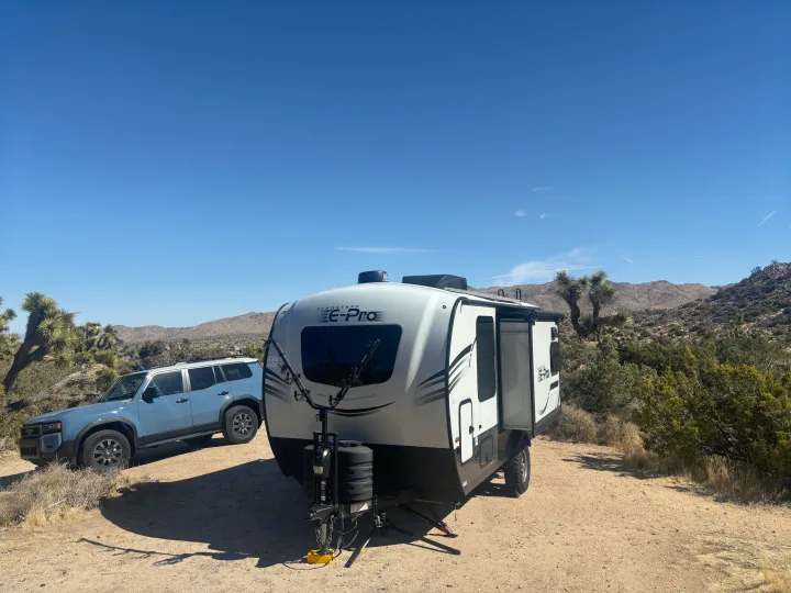 An RV rental travel trailer and SUV parked for desert camping. Perfect for Joshua Tree landscapes and off-grid adventures.. Forest River Flagstaff E-Pro 2024