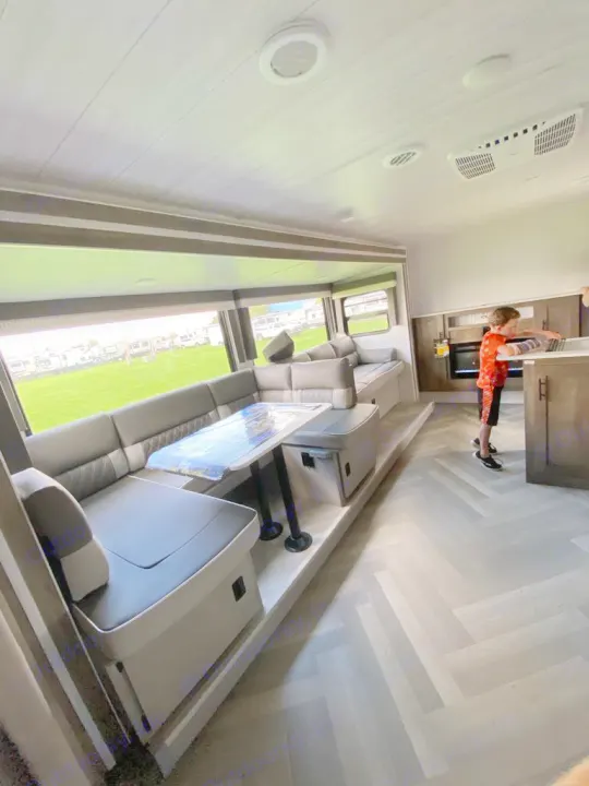 Spacious RV rental interior with a U-shaped dinette, large windows viewing an RV park, and a child by the kitchen.. Forest River Salem Cruise Lite 2022