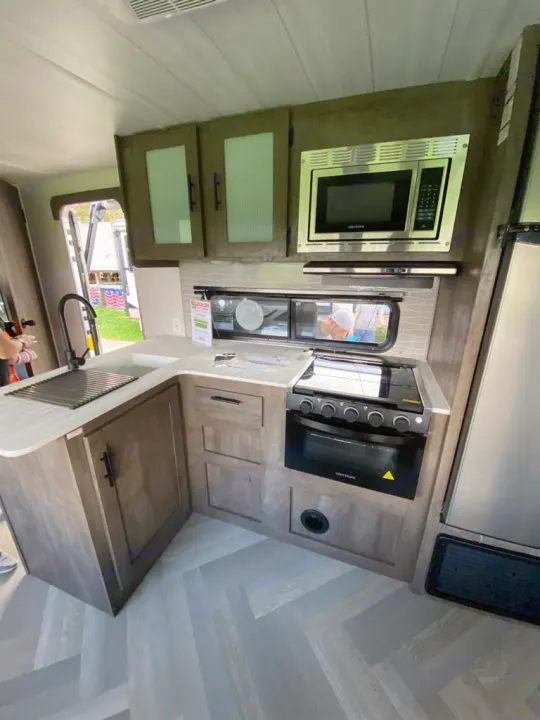 Modern RV rental kitchen: sink, oven, microwave, and light wood-look cabinets on herringbone flooring, ready for trips.. Forest River Salem Cruise Lite 2022