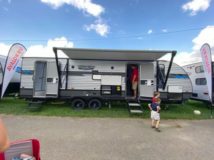 A modern silver travel trailer with an awning extended, showcasing its interior as people explore. Perfect for RV rental adventures!. Forest River Salem Cruise Lite 2022