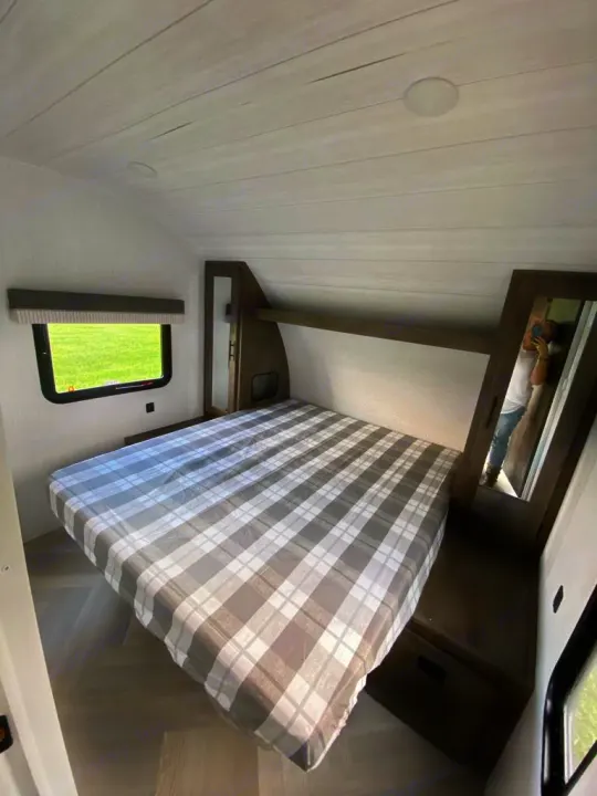 Inside an RV rental: a cozy bedroom featuring a bed with plaid cover, window, and wood-toned storage.. Forest River Salem Cruise Lite 2022