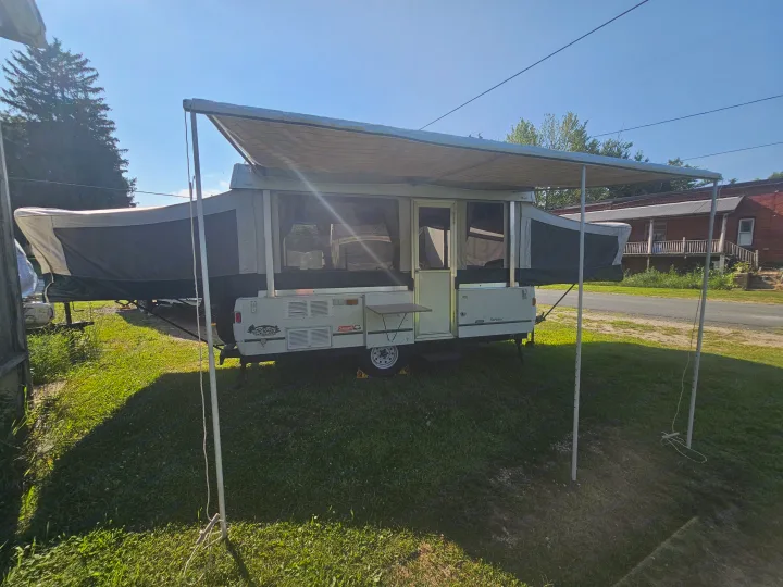 Pop-up RV rental with extended awning, parked on grass. Ready for your outdoor camping adventures!. Coleman Destiny 2000