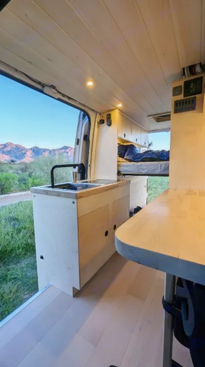 Modern RV rental interior with kitchen, sink, and bed, featuring wood accents and scenic mountain views.. Mercedes-Benz Sprinter 2019