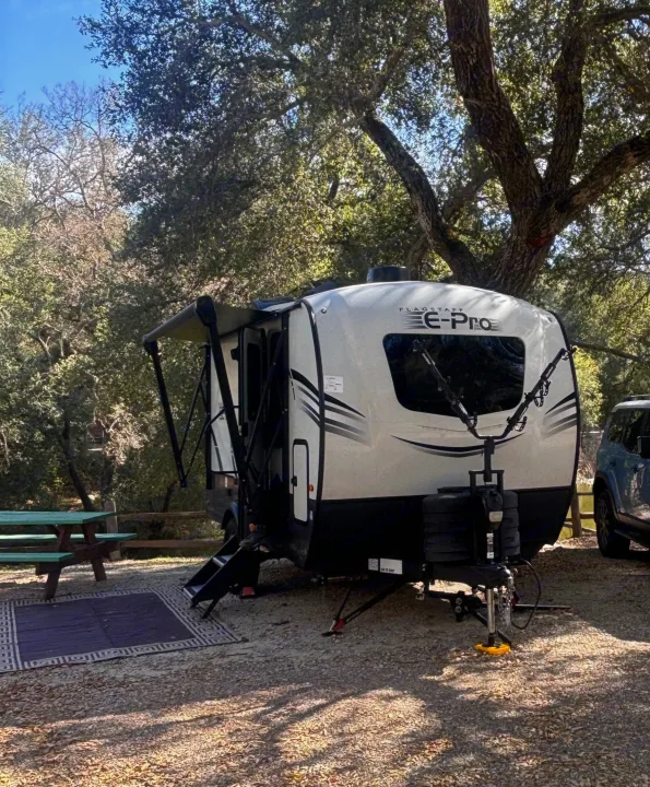 A travel trailer RV rental parked at a serene, tree-shaded campsite with an extended awning and picnic table.. Forest River Flagstaff E-Pro 2024