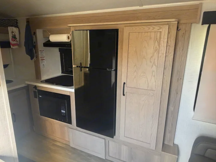 Compact RV rental kitchenette: light wood cabinetry, black fridge, microwave, and cooktop.. Forest River Flagstaff E-Pro 2024