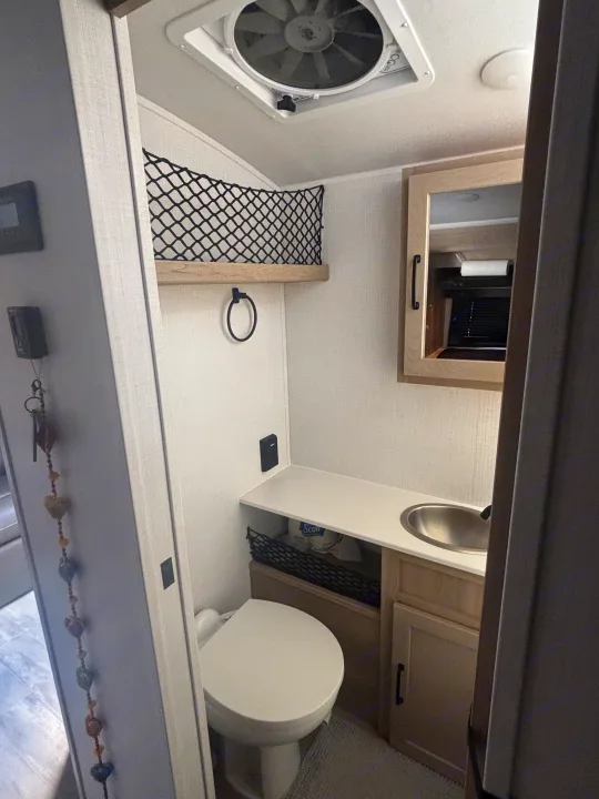 Inside an RV rental: a compact bathroom with a toilet, sink, mirror cabinet, vent fan, and clever storage solutions.. Forest River Flagstaff E-Pro 2024