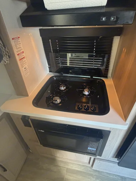 Compact RV rental kitchen, featuring a 3-burner gas stove, microwave, and range hood. Ready for your travels.. Forest River Flagstaff E-Pro 2024