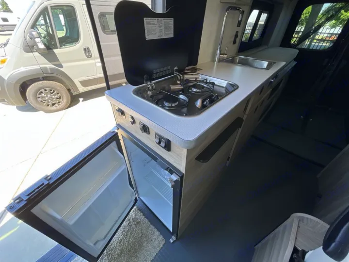 RV rental van kitchen: two-burner stove, sink, and open mini-fridge. Practical interior for adventurers.. Winnebago Solis 2025