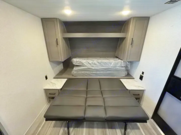 RV rental bedroom with wrapped mattress, overhead storage, and a convertible sofa/bed, perfect for compact travel.. Keystone RV Hideout Sport 2024