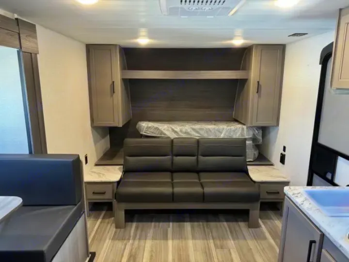 An RV rental's modern interior with a queen bed, sofa, and dining area. Neutral colors throughout.. Keystone RV Hideout Sport 2024