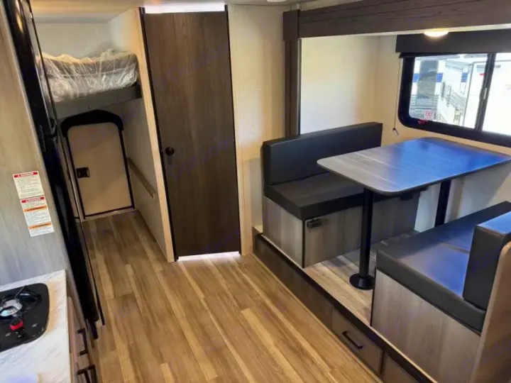 View of an RV rental interior featuring a kitchen with stove, dinette with window, and bunk beds. Compact & functional living.. Keystone RV Hideout Sport 2024