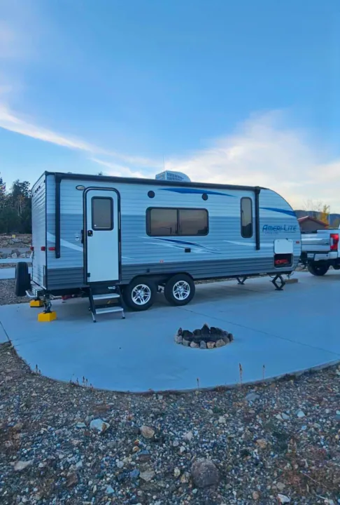 RV rental: An Ameri-Lite travel trailer is set up on a concrete pad with a rock fire pit at a scenic campsite.. Gulf Stream Ameri-Lite 2018