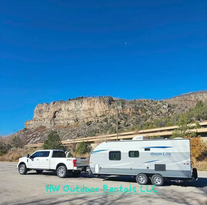 RV rental ready for adventure: White truck & travel trailer in parking lot, mountains & moon in blue sky.. Gulf Stream Ameri-Lite 2018