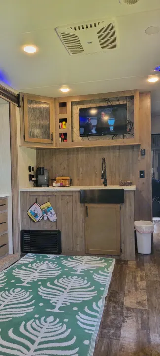 Cozy RV rental kitchen area with a modern sink, coffee maker, TV, and a vibrant green rug.. Forest River Cherokee Wolf Pack 2021