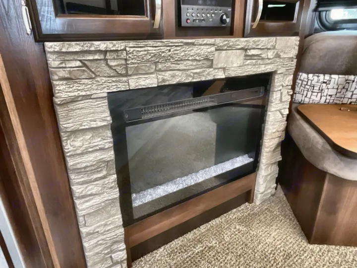 Cozy RV rental interior featuring an electric fireplace with a stone surround, entertainment center, and comfy dinette seating.. Jayco White Hawk 2019