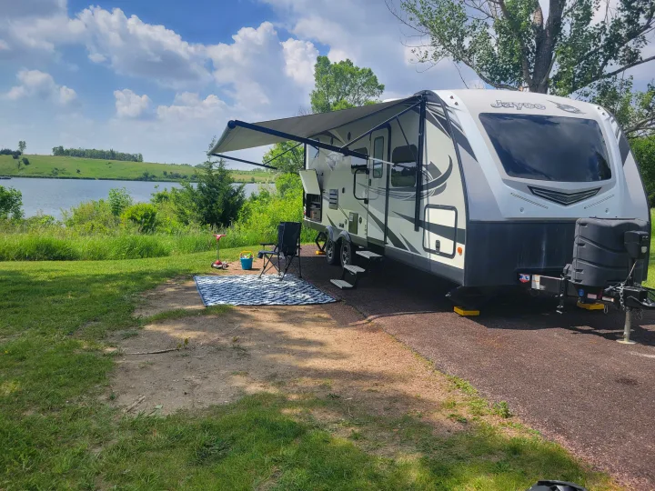 Relaxing RV rental setup: A travel trailer with an extended awning at a scenic lakeside campsite.. Jayco White Hawk 2019