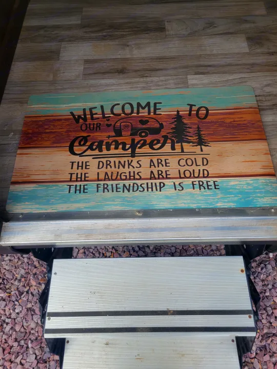 RV rental entrance: A welcome mat reads "Welcome to our Camper," with steps and gravel visible below.. Jayco White Hawk 2019