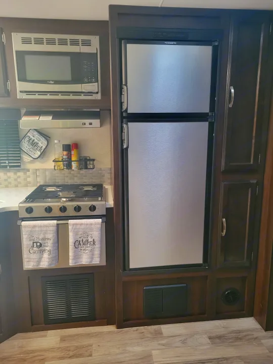 Inside an RV rental: a cozy kitchen with stainless steel microwave, Dometic fridge & stove, and camping decor.. Jayco White Hawk 2019