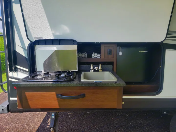 This RV rental features a convenient outdoor kitchen with a stove, sink, and refrigerator, perfect for camping.. Jayco White Hawk 2019
