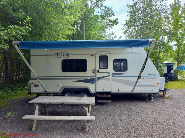 This RV rental is set up at a treed campground with its blue awning extended and a wooden picnic table ready.. Terry Dakota 722F 2004