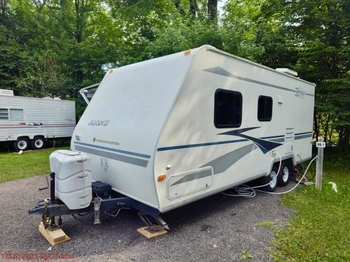 A white Terry Dakota travel trailer, ideal for an rv rental, is parked at a shaded campsite with utility hookups.. Terry Dakota 722F 2004