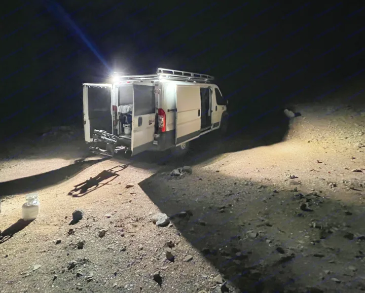 An RV rental camper van parked outdoors at night, with interior lights on and rear doors open, illuminating the surrounding rocky ground.. Custom Ram Promaster 1500 2017
