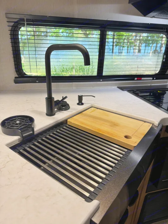 RV rental kitchen showcasing a modern sink with black faucet, built-in soap dispenser, cup rinser, roll-up drying rack, and cutting board.. Forest River Cherokee Grey Wolf 2024