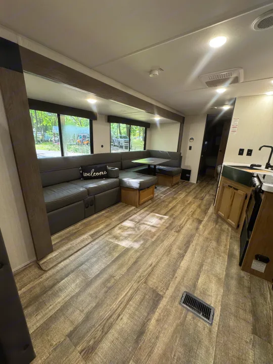 RV rental interior: A bright, spacious living area with a U-shaped dinette, kitchen, and large windows revealing a campsite view.. Forest River Cherokee Grey Wolf 2024