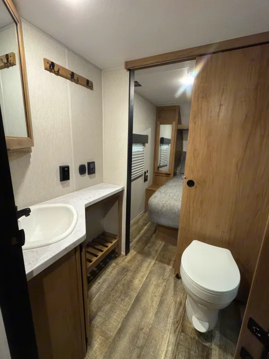 RV rental's functional bathroom with sink & toilet, plus a glimpse of the bedroom through a sliding door.. Forest River Cherokee Grey Wolf 2024