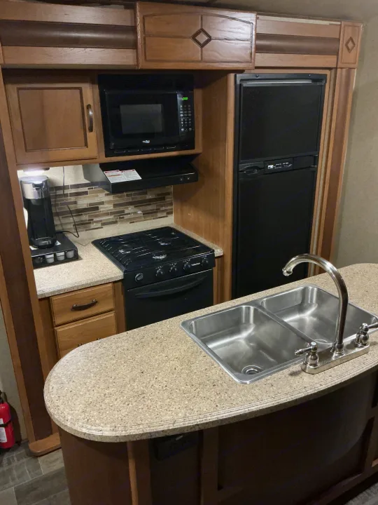Well-equipped RV rental kitchen: microwave, stove, fridge, double sink, and coffee maker on granite-look counter.. Crossroads RV Sunset Trail Super Lite 2017