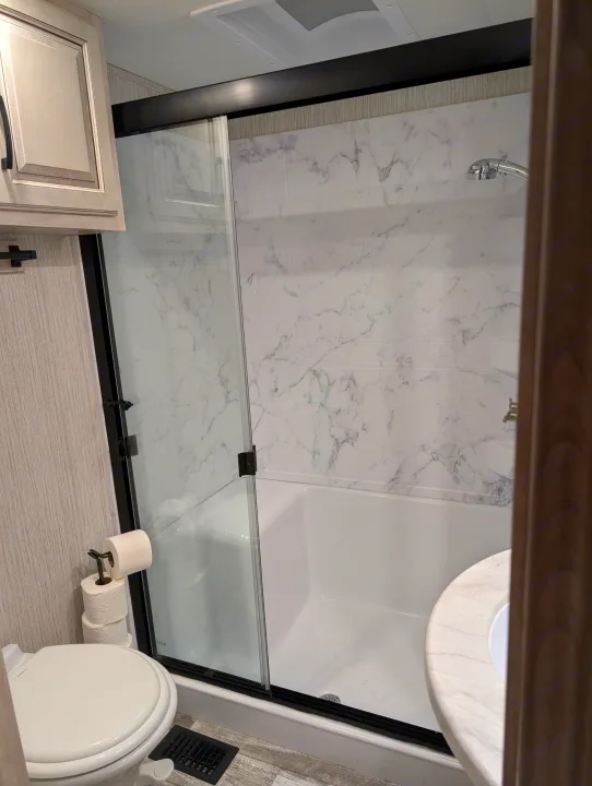 Clean and modern RV rental bathroom featuring a shower with black-framed glass doors, toilet, and elegant marble-look walls.. Forest River Sandpiper 2022