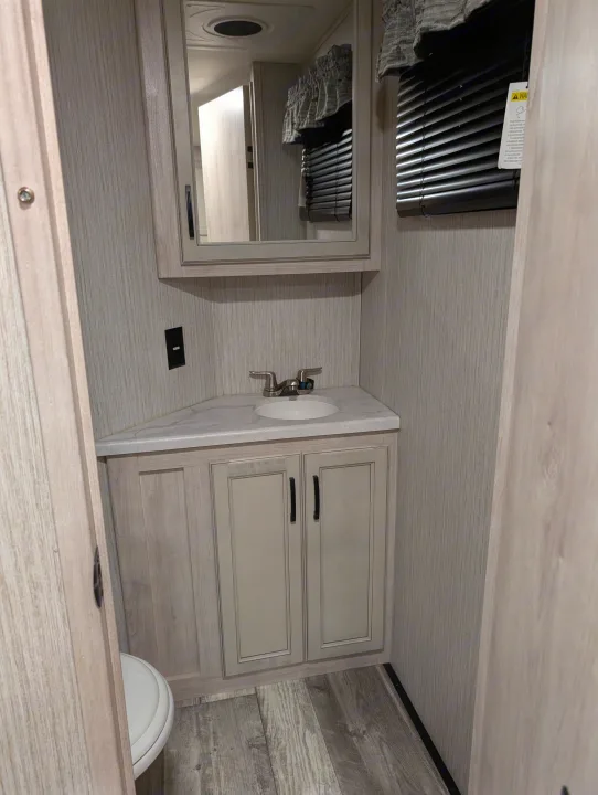 Compact RV rental bathroom with corner vanity, sink, mirror, and wood-grain interior.. Forest River Sandpiper 2022