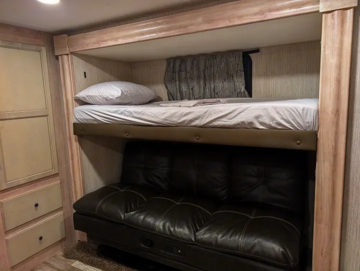 This modern RV rental features a cozy bunk bed over a comfortable dark leather sofa and built-in storage for efficient living space.. Forest River Sandpiper 2022
