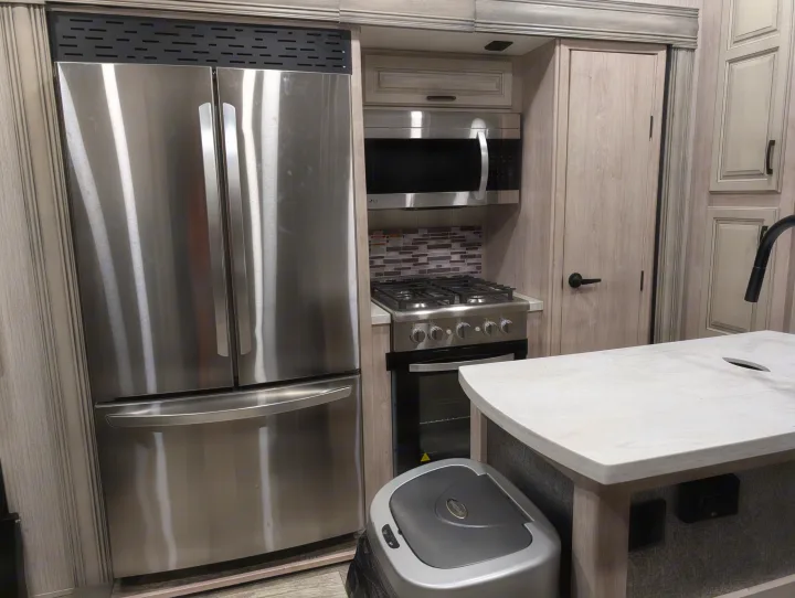 Sleek RV rental kitchen: stainless steel refrigerator, LG microwave, gas range, and light wood cabinets.. Forest River Sandpiper 2022