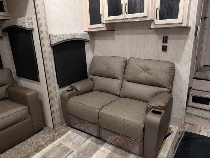 Inside an RV rental: plush gray recliners with cup holders, light wood walls, and functional cabinets.. Forest River Sandpiper 2022