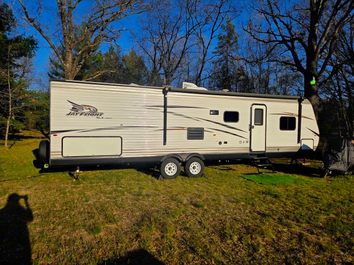 White Jay Flight travel trailer RV rental set up in a grassy, treed campsite under clear skies.. Jayco Jay Flight SLX 2018