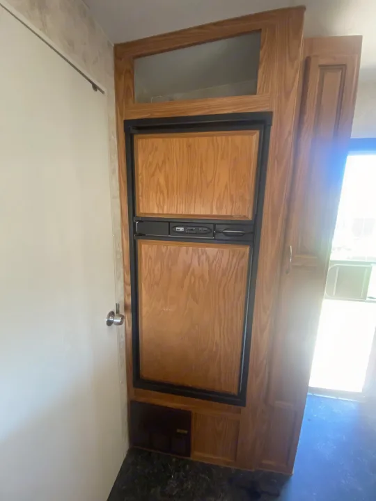 Inside an RV rental, featuring a wood-paneled refrigerator, surrounding cabinetry, and a bright window.. Eclipse Recreational Vehicles Attitude 2006