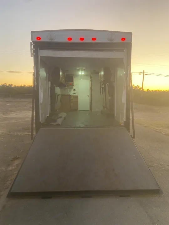 Inside an RV rental, the ramp door is open, showing a functional mobile living space with cabinets & a sink during sunset.. Eclipse Recreational Vehicles Attitude 2006