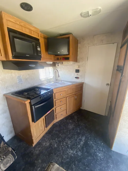 An efficient RV rental kitchen showcasing a microwave, stove, double sink, and warm wood cabinetry with a speckled floor.. Eclipse Recreational Vehicles Attitude 2006