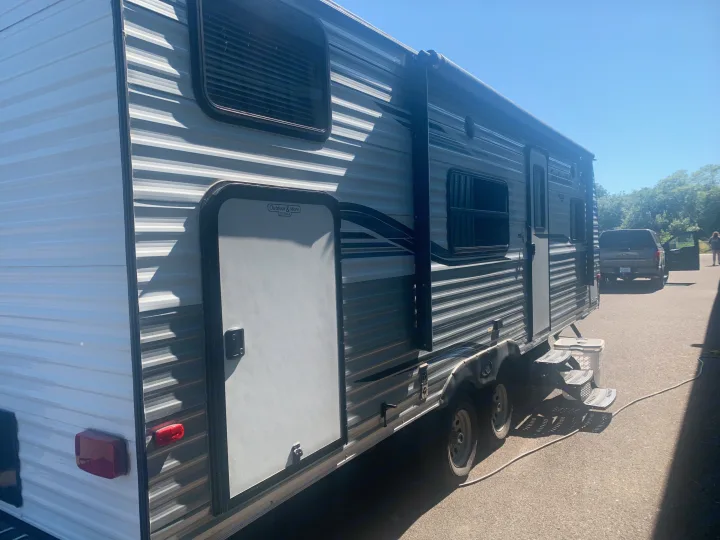 Side view of a grey striped RV rental or travel trailer parked outdoors, showing windows, doors, and a rolled awning.. Keystone RV Springdale 2019
