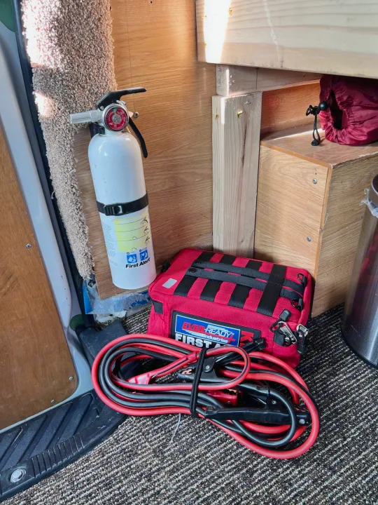 RV rental interior shows essential safety gear: a white mounted fire extinguisher, red first aid kit, and jumper cables on the floor.. Ford Econolline 250s 2006