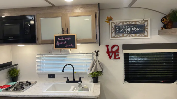 Cozy RV rental kitchen featuring a microwave, sink, two-burner stove, and charming decor like the 'Happy place' sign.. Gulf Stream Grand River 22Mb 2024