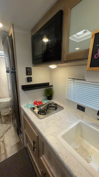 This RV rental features a modern kitchenette with a stove, microwave, sink, and fridge, optimizing space for travel.. Gulf Stream Grand River 22Mb 2024