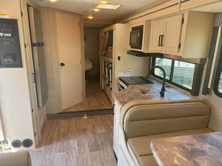This rv rental interior features a kitchen with dinette, control panel, refrigerator, and bunk beds, offering a spacious travel experience.. Thor Chateau 2023